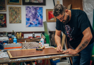 Artiste peintre travaillant sur l'encadrement d'une toile dans son atelier, illustrant le travail de création en coulisses nécessaire pour se faire connaître en tant qu'artiste.