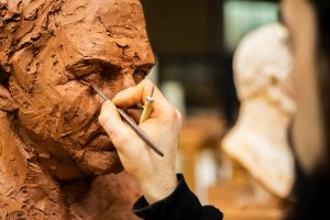 Hand of sculptor finishing a clay head eye in an art studio