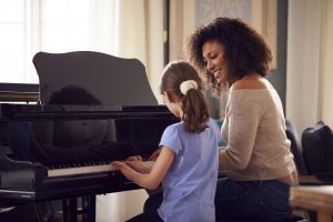 Young Girl Learning To Play Piano Having Lesson From Female Teacher